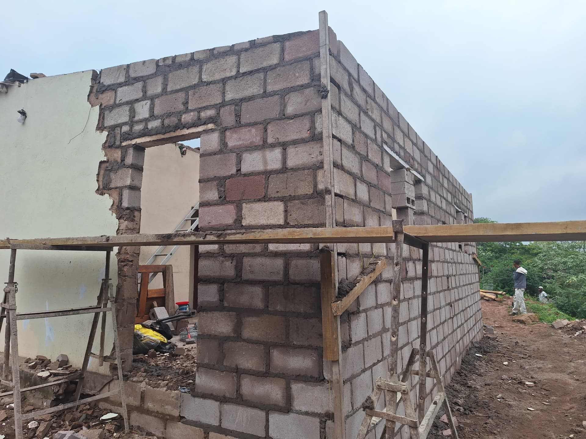 New grey concrete block walls rising beside the existing pale green house, with scaffolding in place